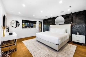 A modern bedroom with a large bed, a bedside table, a mirror, and a view of the outside. - Caverna Estate (Los Angeles)