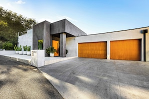 Uma casa moderna de dois andares, com fachada de concreto, entrada por automóvel e duas garagens.