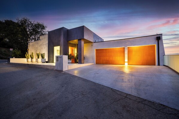 A modern building with a garage door, a driveway, and a row of cacti. - Caverna Estate (Los Angeles)