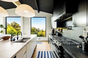 A modern kitchen with a large island, a gas stove, and a view of the outdoors. - Caverna Estate (Los Angeles)