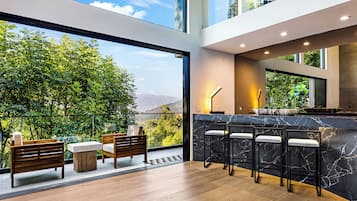 A modern interior with a bar area, seating, and large windows offering a view of greenery and mountains.