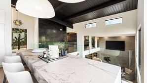 Une cuisine moderne dotée d’un plan de travail en marbre, de luminaires suspendus et offrant une vue sur l’extérieur.