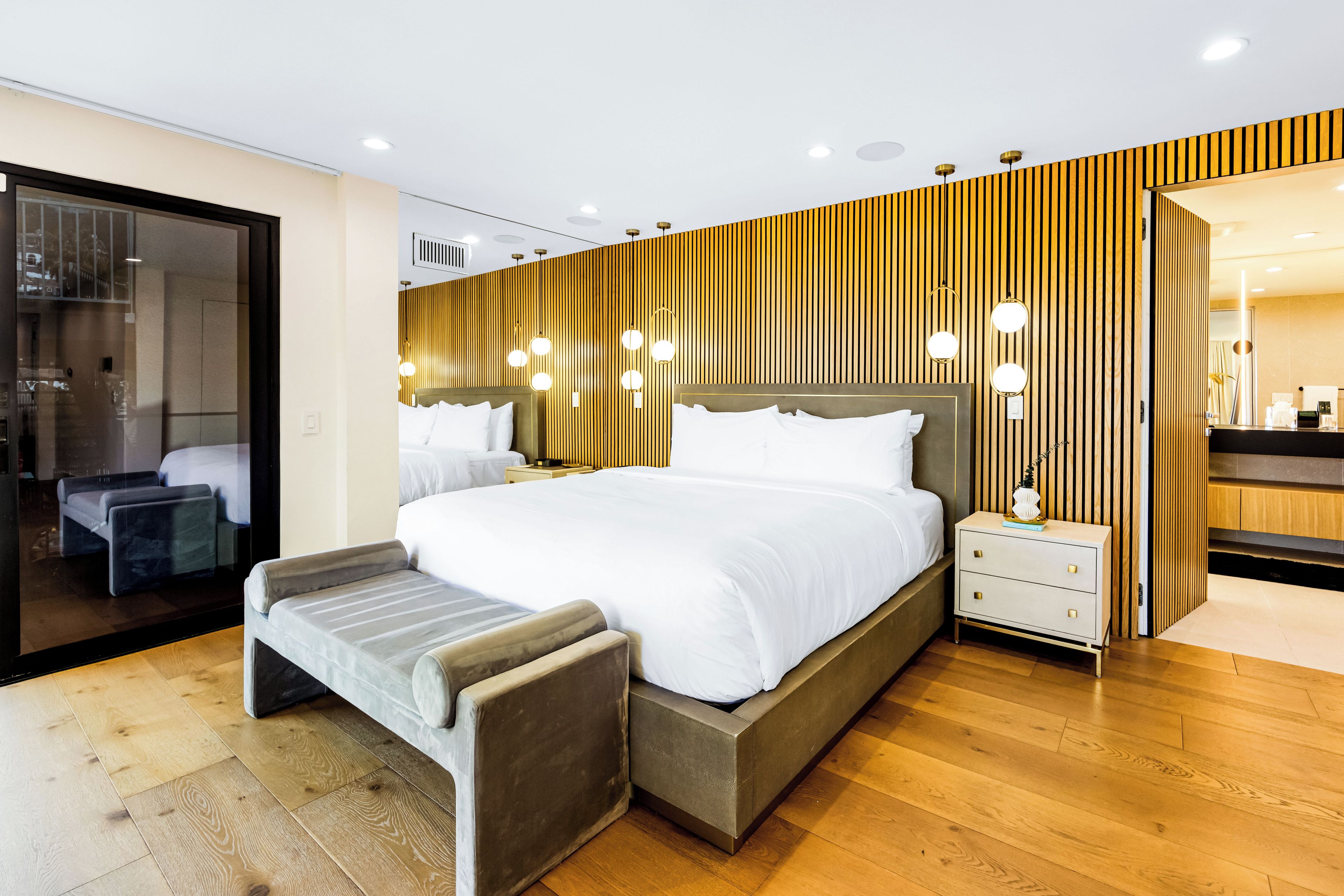 Una habitación de hotel moderna con una cama grande, mesitas de noche, un banco y vistas a la ciudad.