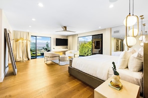 A modern hotel room with a large bed, a desk, a chair, and a view of the outdoors. - Caverna Estate (Los Angeles)