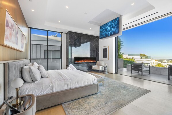 A modern bedroom with a large bed, a fireplace, and a balcony with outdoor seating. - Sierra Mar (West Hollywood)