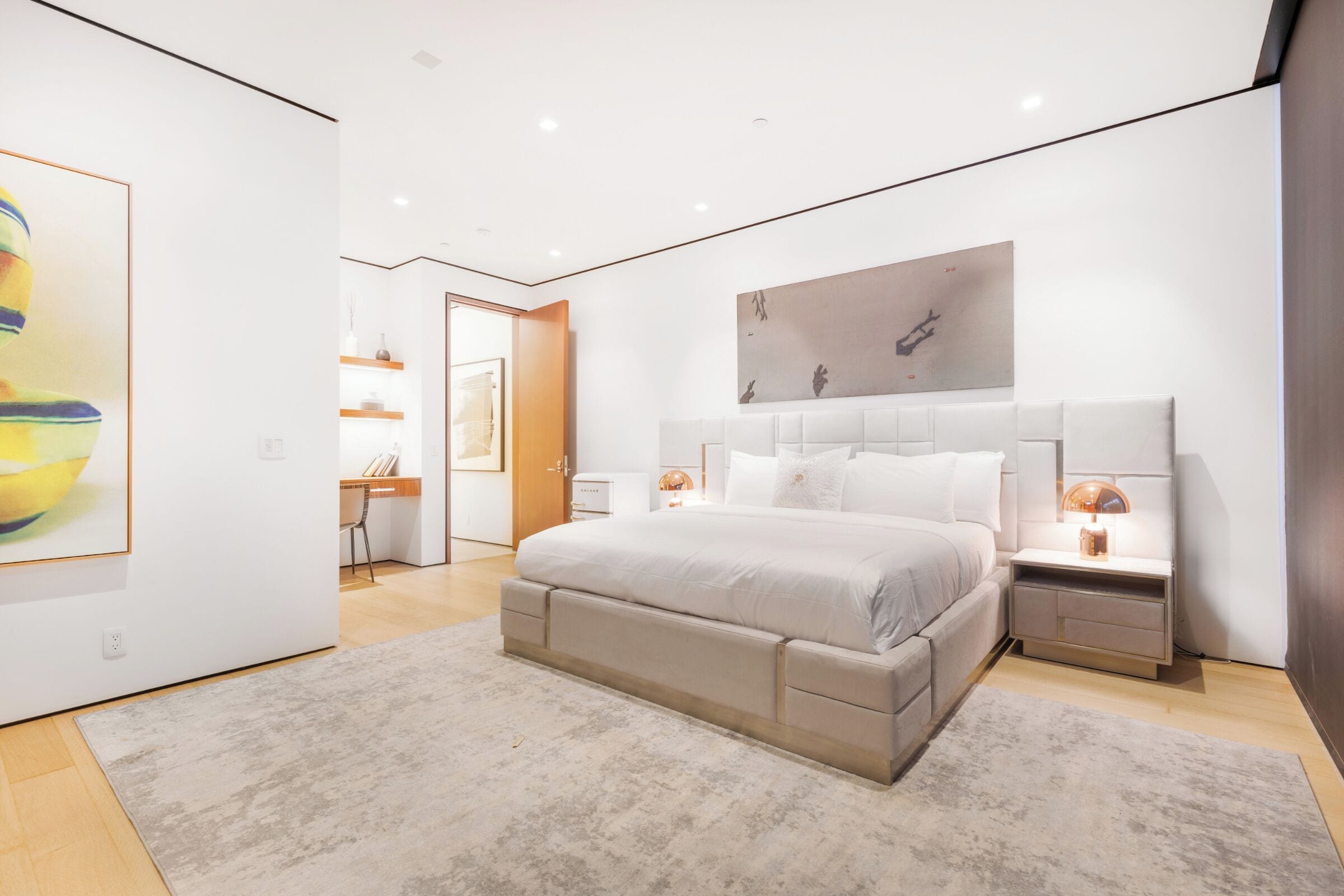 Un dormitorio moderno con una cama grande, mesitas de noche y obras de arte en las paredes.