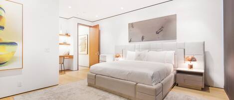 Un dormitorio moderno con una cama grande, mesitas de noche y obras de arte en las paredes.