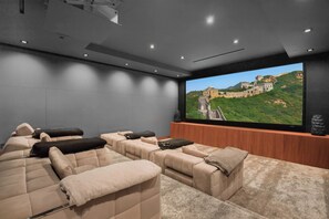 A home theater with a large screen displaying a scenic view, plush seating, and a modern ceiling design. - Sierra Mar (West Hollywood)