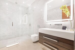 Un baño moderno con ducha envuelta en vidrio, un inodoro blanco, un tocador con espejo y un florero con flores.