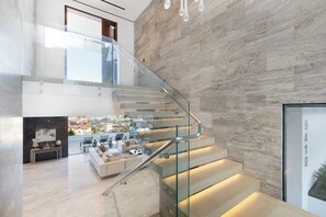 A modern interior with a glass staircase, a city view, and a living area with sofas and a coffee table. - Sierra Mar (West Hollywood)