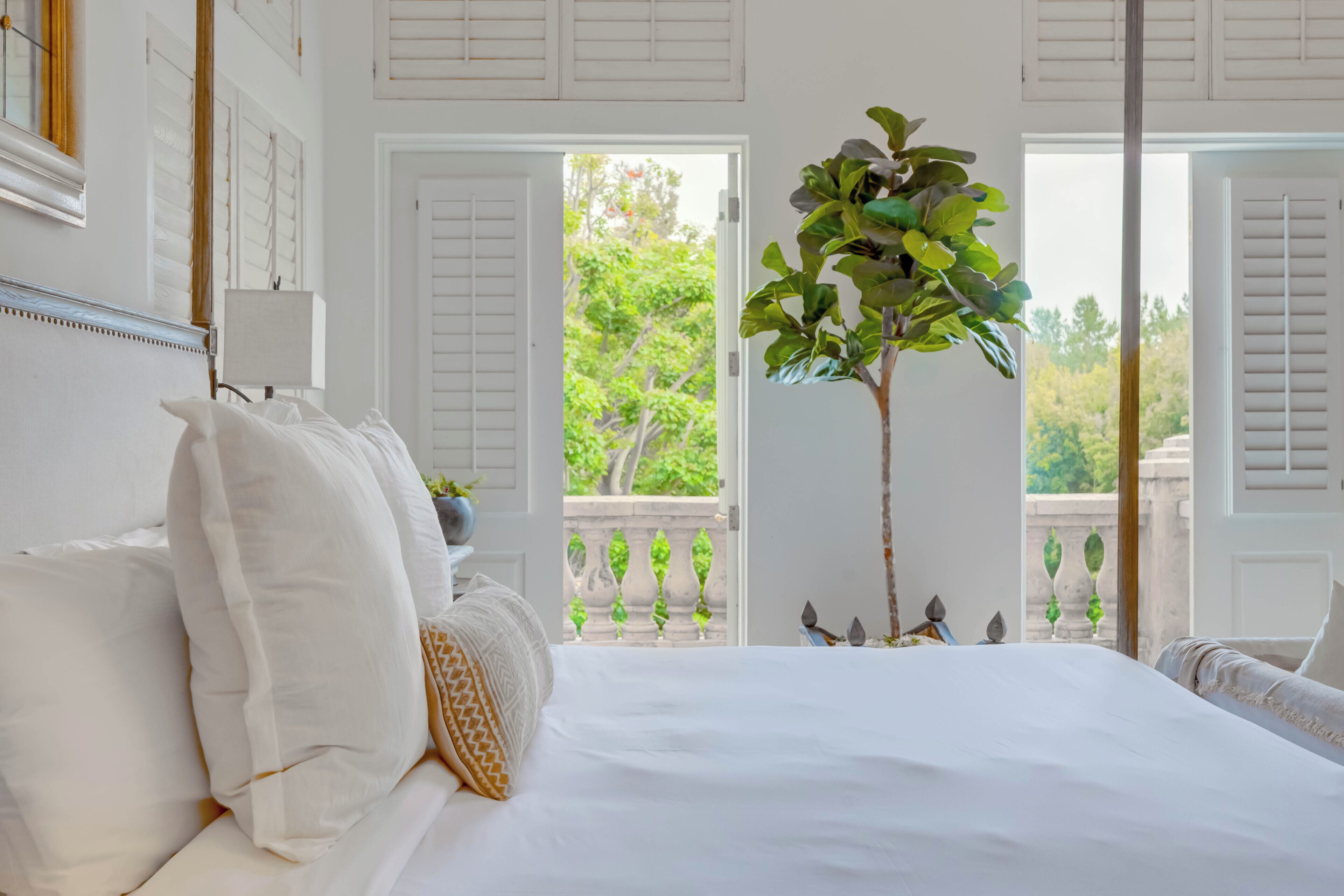 Quarto com cama grande, paredes brancas e varanda com vista para o verde.