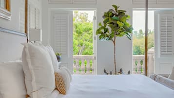 Quarto com cama grande, paredes brancas e varanda com vista para o verde.