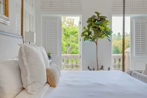 Quarto com cama grande, paredes brancas e varanda com vista para o verde.