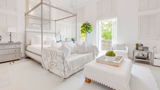 A white four-poster bed with a canopy, a white sofa, a small side table with a plant, and a view of greenery outside. - Carolwood Estate (Beverly Hills)