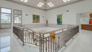 A spacious room with a high ceiling, skylights, and a central open area surrounded by a metal railing. - Carolwood Estate (Beverly Hills)
