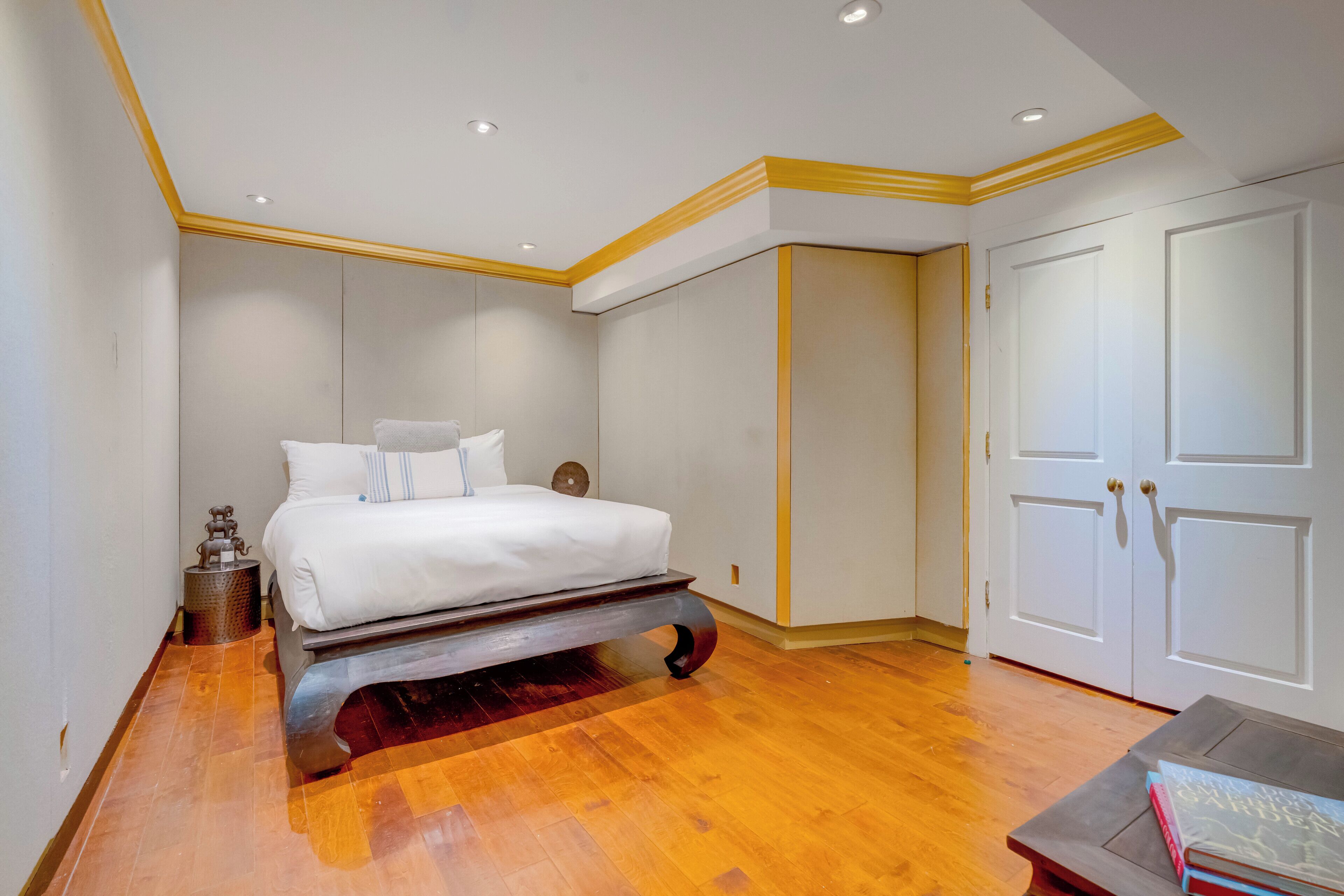 Quarto com cama, soalho de madeira, paredes brancas e guarda-roupa.