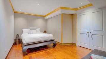 Quarto com cama, soalho de madeira, paredes brancas e guarda-roupa.
