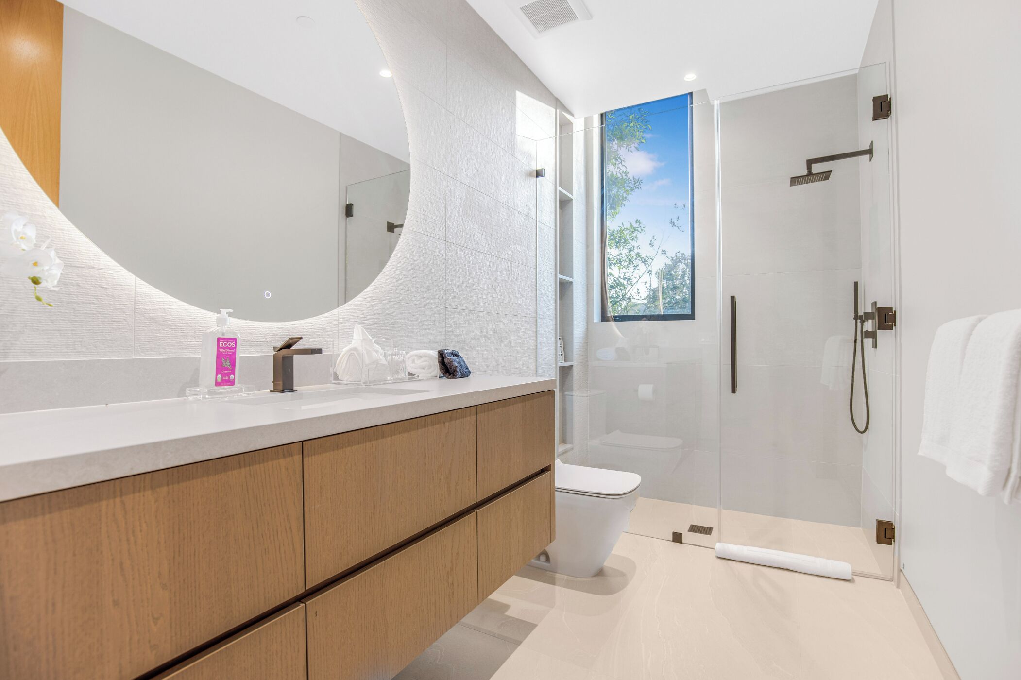 A modern bathroom with a curved mirror, a shower enclosure, and a toilet.