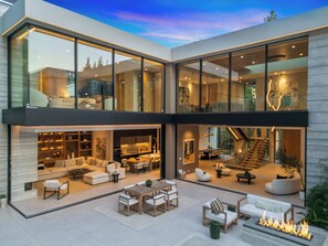 A modern two-story house with a spacious outdoor patio, a dining area, and a staircase leading to an upper level. - Hutton Modern (Beverly Hills)