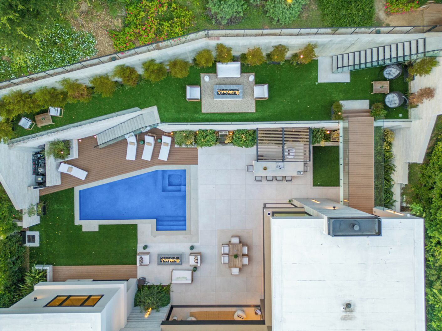 An aerial view of a modern outdoor living area with a swimming pool, sun loungers, a barbecue area, and a covered seating area.