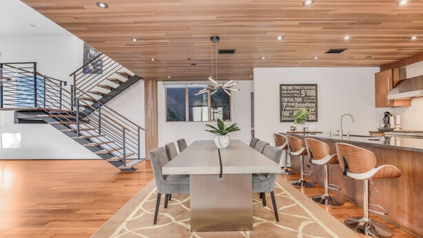 A modern dining area with a long table, bar stools, and a staircase. - Cedar Loft Villa (Venice)