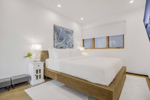 A modern bedroom with a wooden bed frame, white bedding, a nightstand with a lamp, and a wall-mounted artwork. - Cedar Loft Villa (Venice)