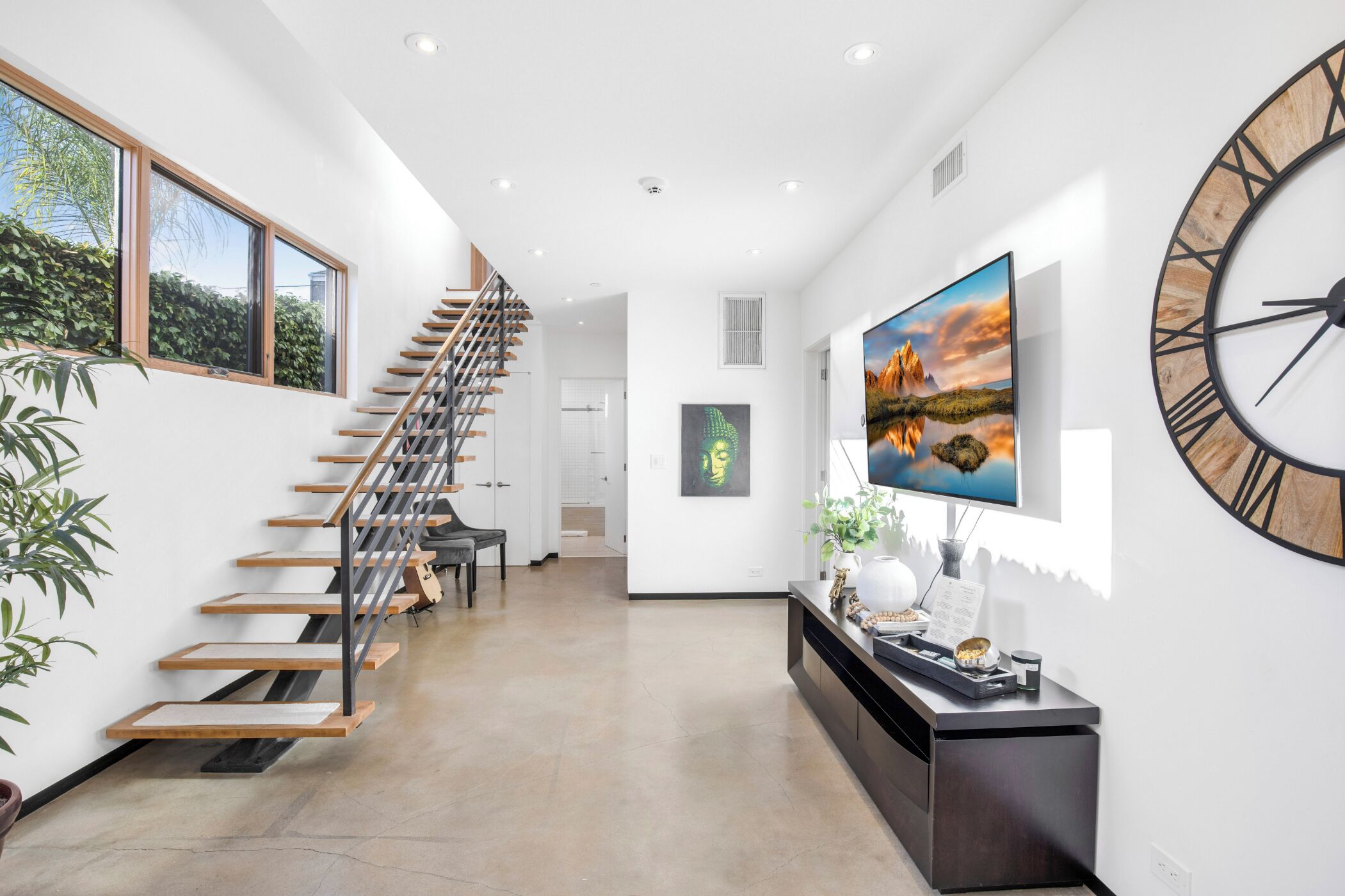 A modern interior with a staircase, a large wall clock, and artwork.