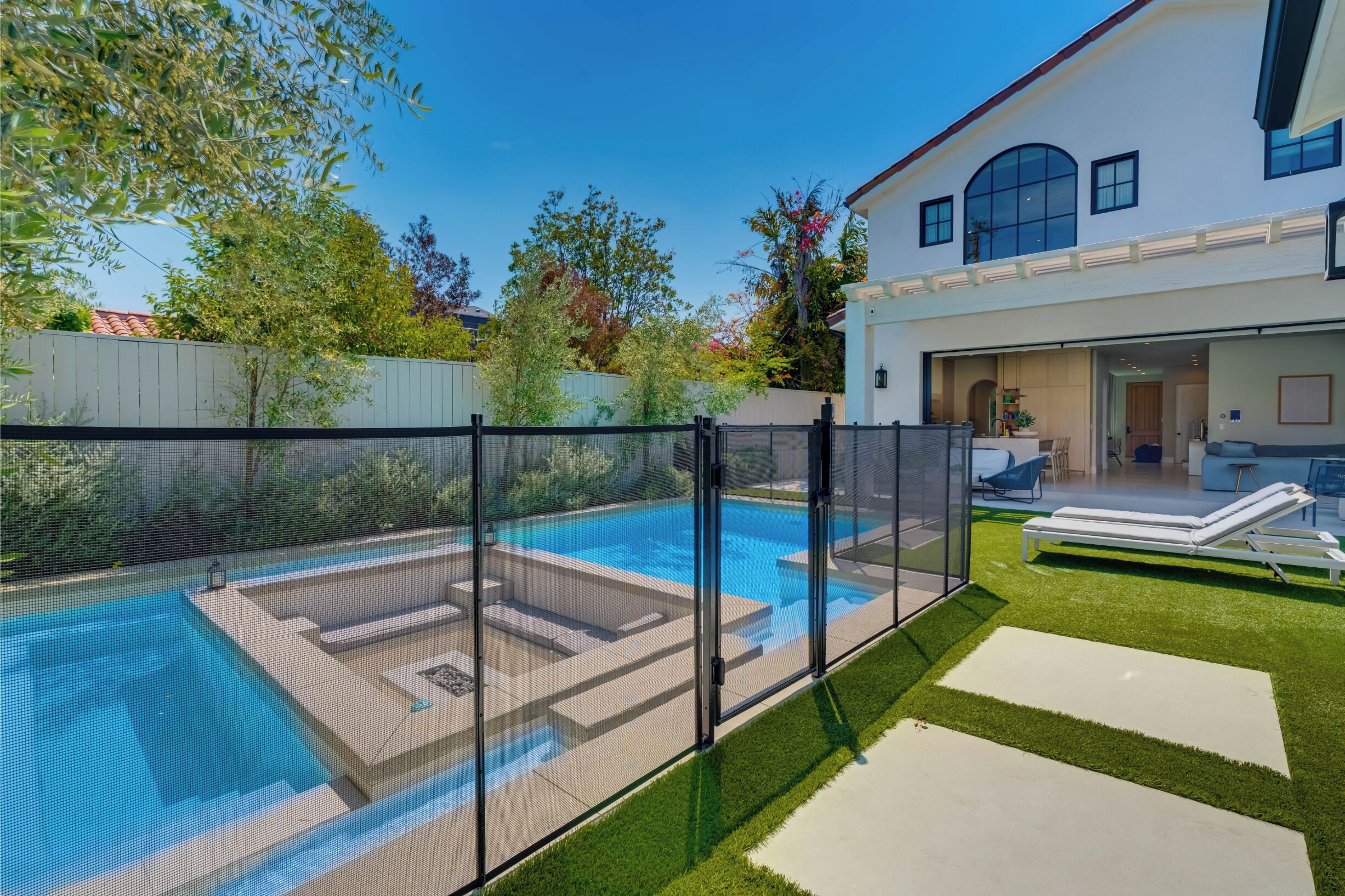 A backyard with a swimming pool, a fenced area, and a house with a covered patio.