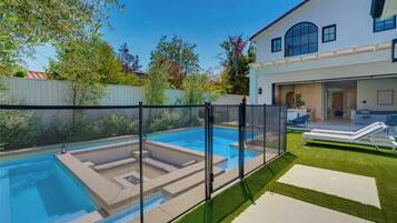 A backyard with a swimming pool, a fenced area, and a house with a covered patio.