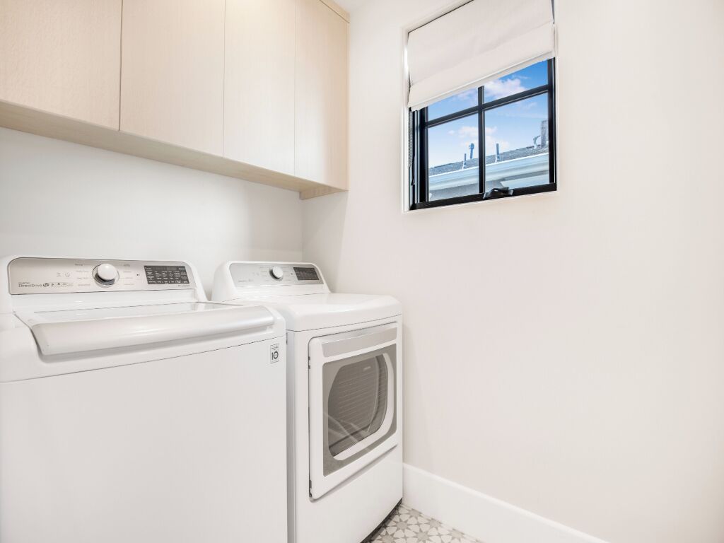 A laundry room with two white washing machines and a dryer, a window with a view of a bridge, and light-colored walls and floor.