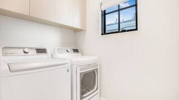 A laundry room with two white washing machines and a dryer, a window with a view of a bridge, and light-colored walls and floor.