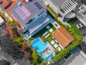 An aerial view of a modern house with a swimming pool, solar panels, and a covered patio.