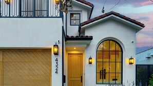 A two-story house with a garage, a large arched window, and a door with a number plaque. - Villa Camellia (Studio City)