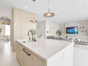 Una cocina moderna con una isla grande, iluminación colgante y vistas al mar a través de una ventana.