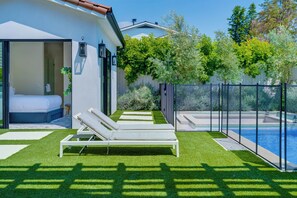 A modern outdoor pool area with a lounge chair, a bed, and a view of the pool.