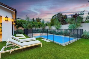 A backyard with a swimming pool, artificial grass, and a white building with a balcony.