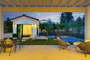 A modern house with a swimming pool, outdoor seating, and a well-lit interior.