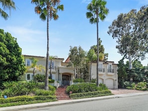 A two-story house with a front entrance, a driveway, and a well-maintained garden with palm trees and shrubs. - Savona Sanctuary Estate (Los Angeles)