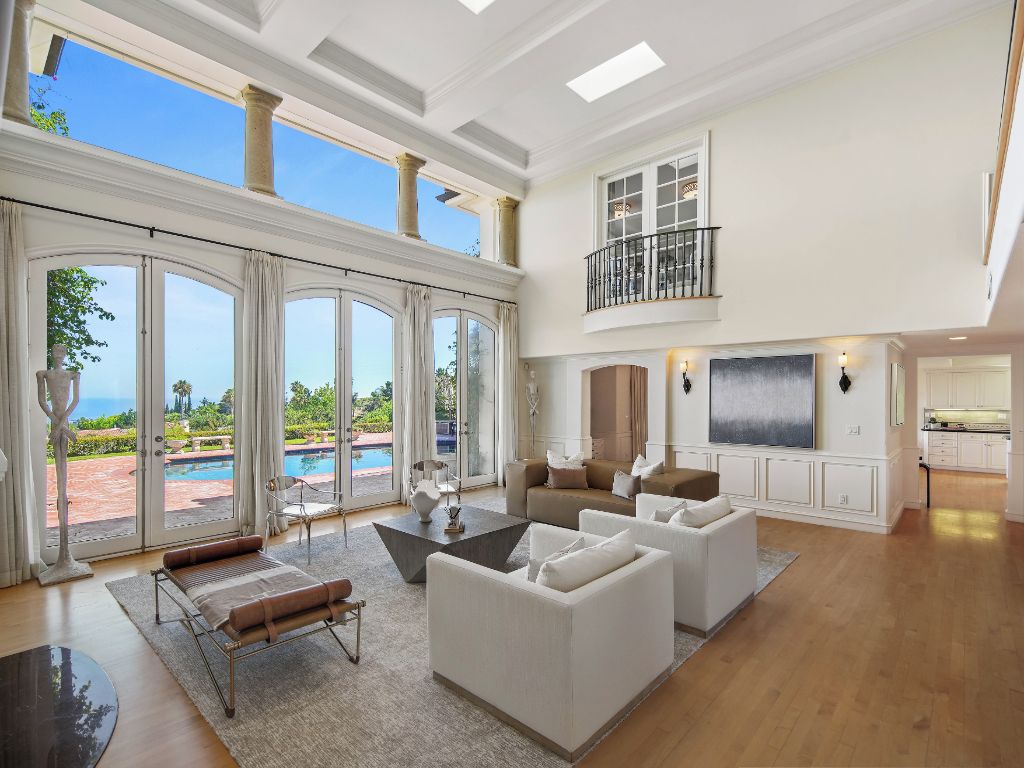 A spacious living room with a large window overlooking a pool, a balcony, and a kitchen area.