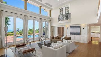 A spacious living room with a large window overlooking a pool, a balcony, and a kitchen area.