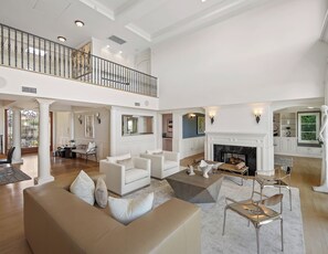 A spacious living area with a high ceiling, a fireplace, and a balcony.