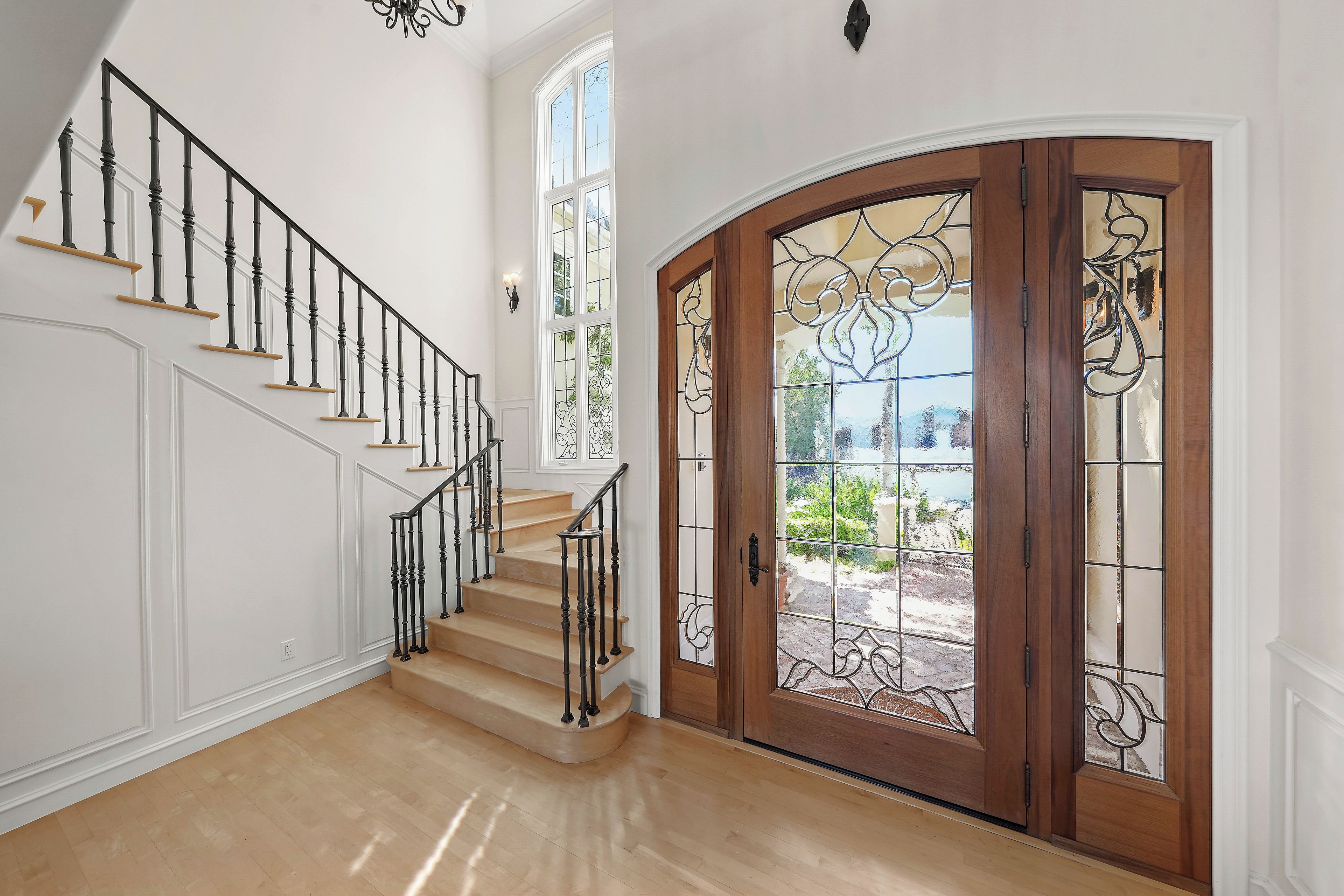 A staircase with black balusters and wooden steps, leading to a door with stained glass panels.