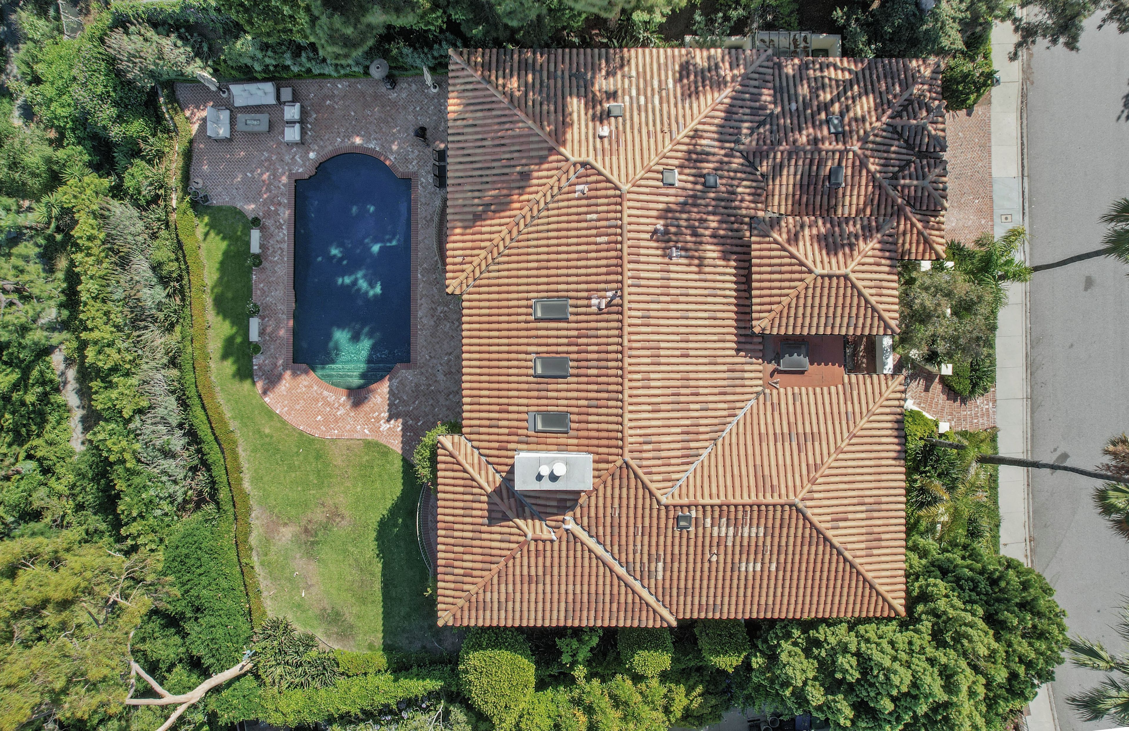 An aerial view of a house with a swimming pool, a patio with outdoor furniture, and a tiled roof.