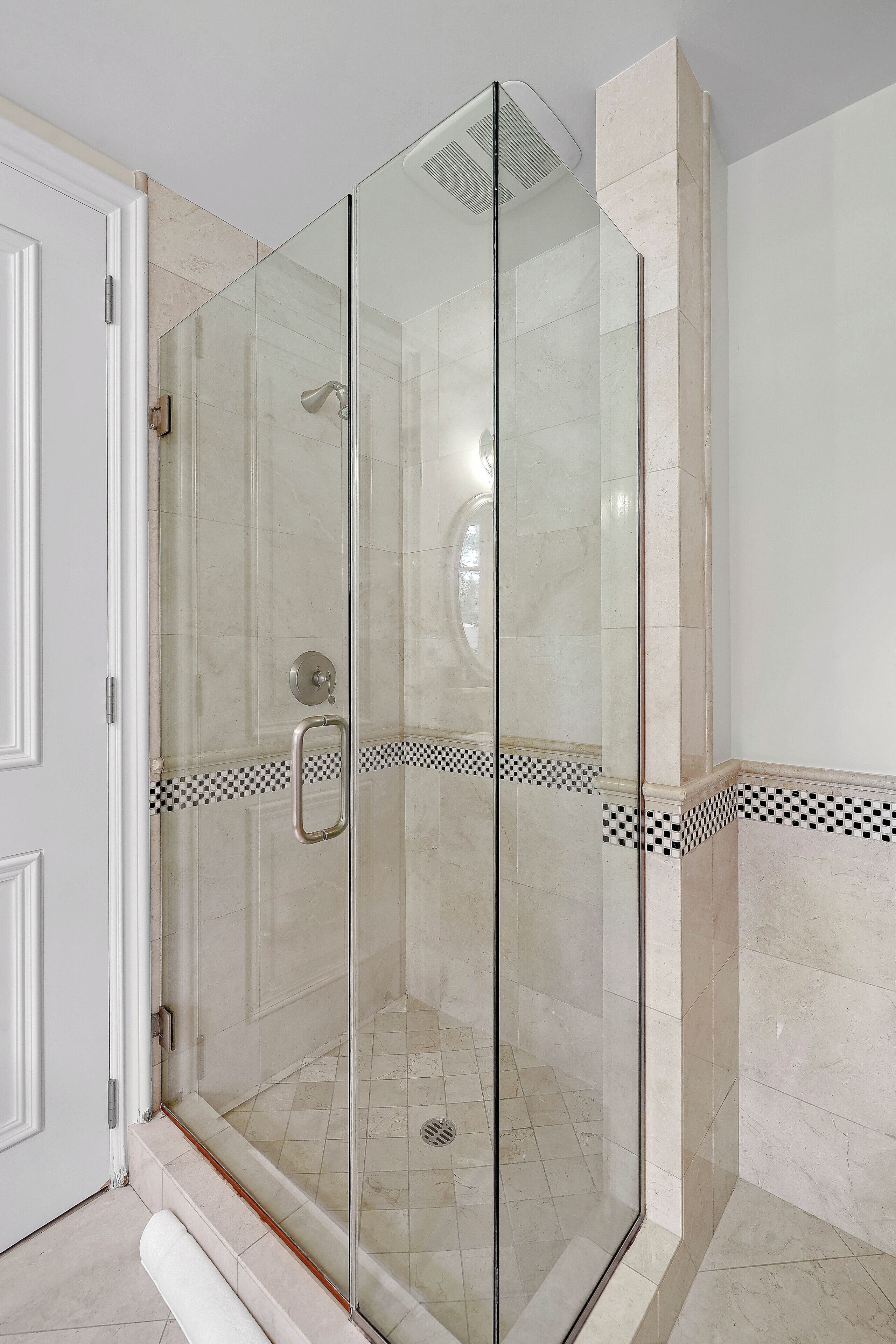 A glass-enclosed shower area with a tiled floor and a checkered border detail.