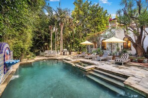 A pool area with clear water, surrounded by lush greenery and a white building with windows. - Sunset Vale (West Hollywood)