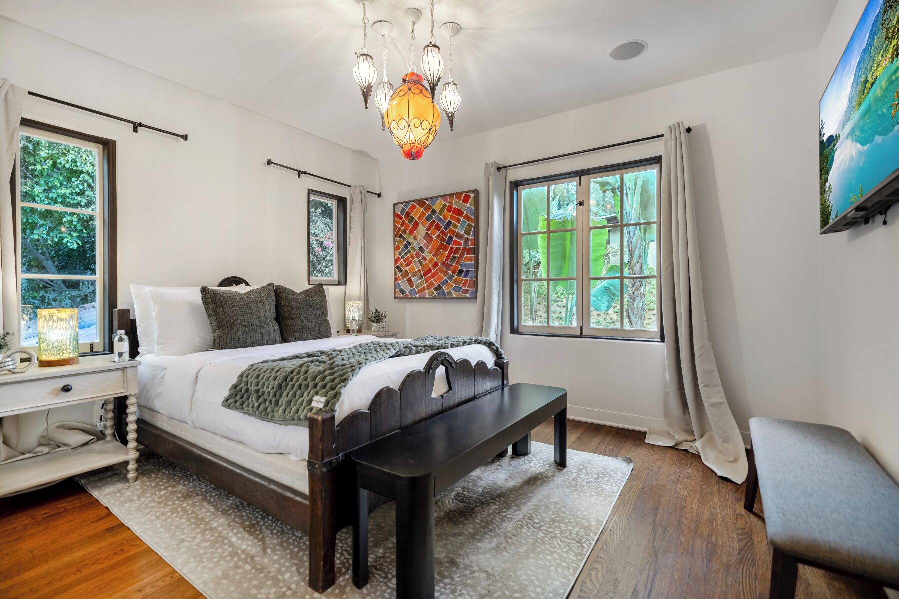A bedroom with a bed, bedside table, bench, and a large window with curtains.