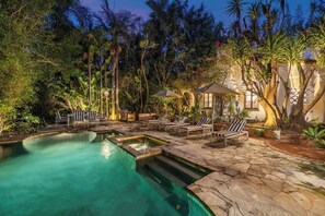 A pool area with lounge chairs and umbrellas, surrounded by tropical plants and a stone deck. - Sunset Vale (West Hollywood)