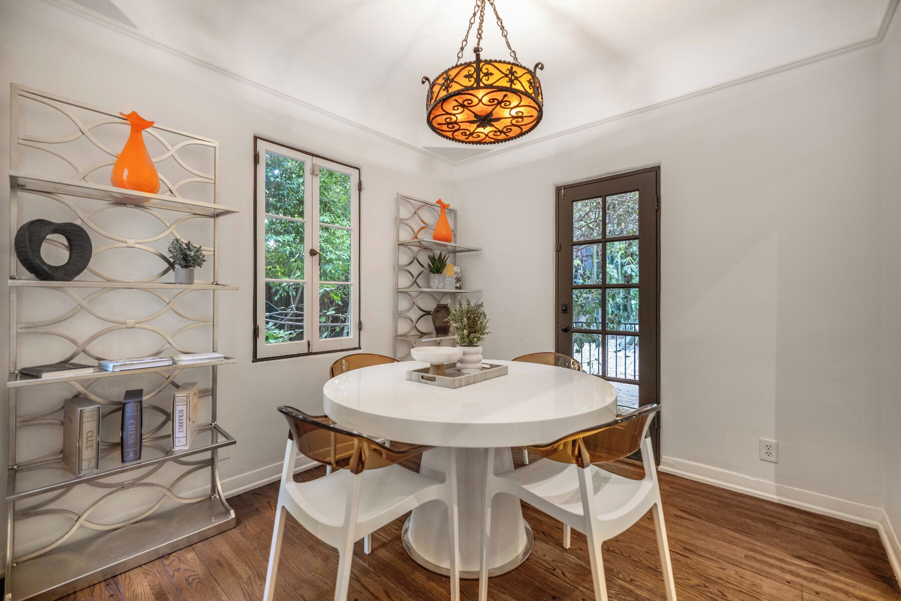 A dining area with a round table, white chairs, a chandelier, and shelves with decorative items.