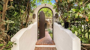 A covered brick pathway leading to a white-walled building with a large wooden door. - Sunset Vale (West Hollywood)