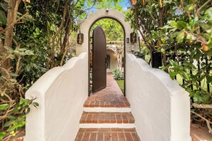 A covered brick pathway leading to a white-walled building with a large wooden door. - Sunset Vale (West Hollywood)